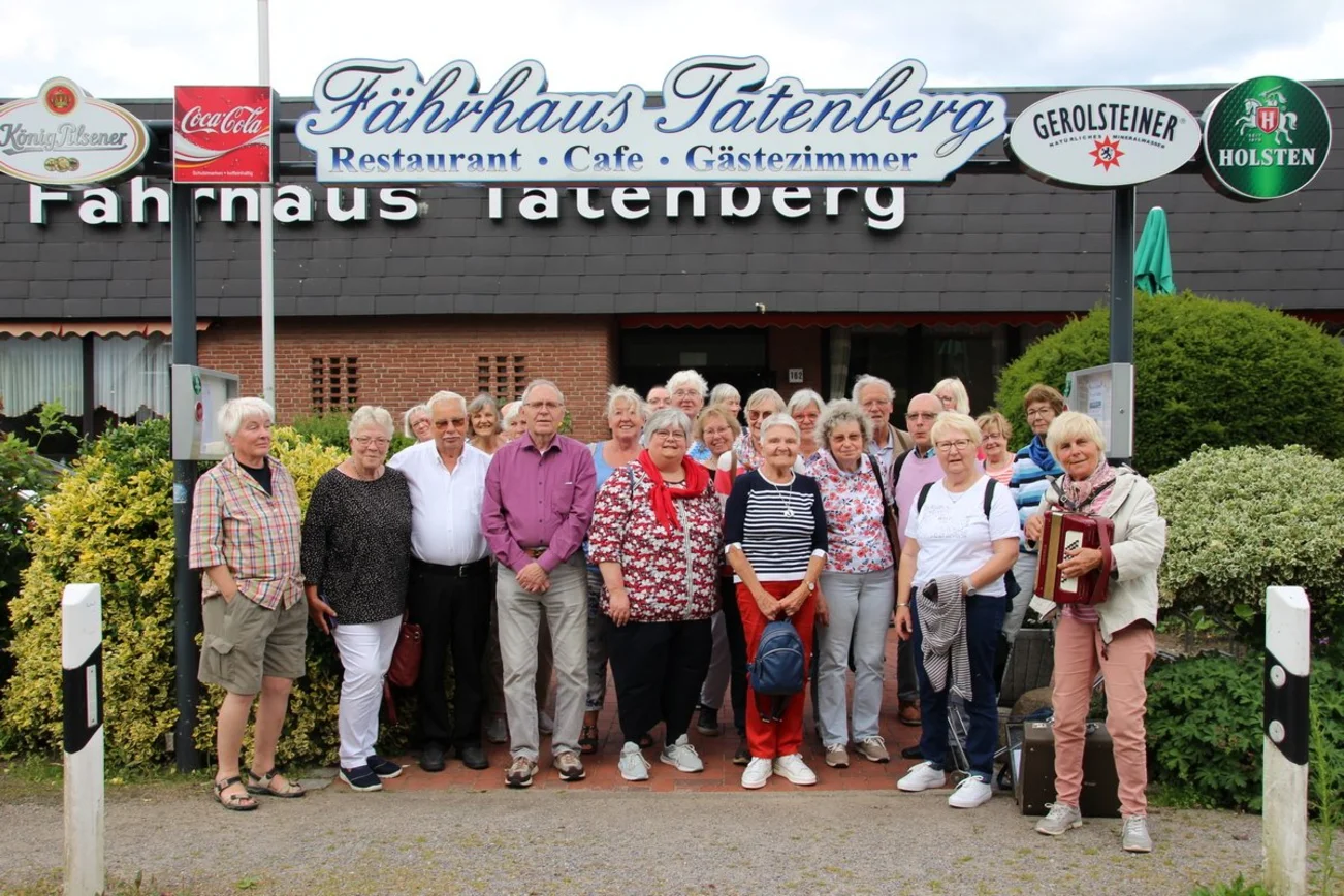 Die ehrenamtlich engaierten Menschen stehen vor einem Lokal und schauen in die Kamera.