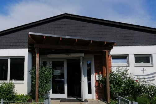 Weißes Haus mit dunklem Dach und offener Eingangstür mit Vordach