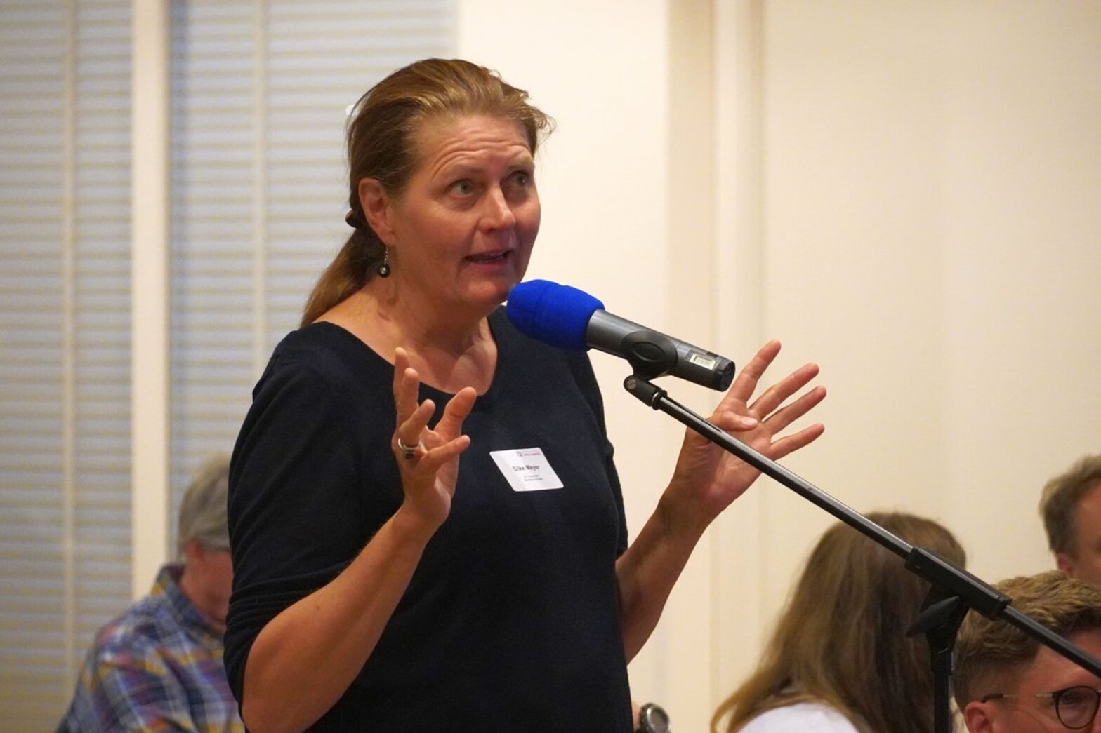 Eine Frau steht gestikulierend an einem Mikrofon. 