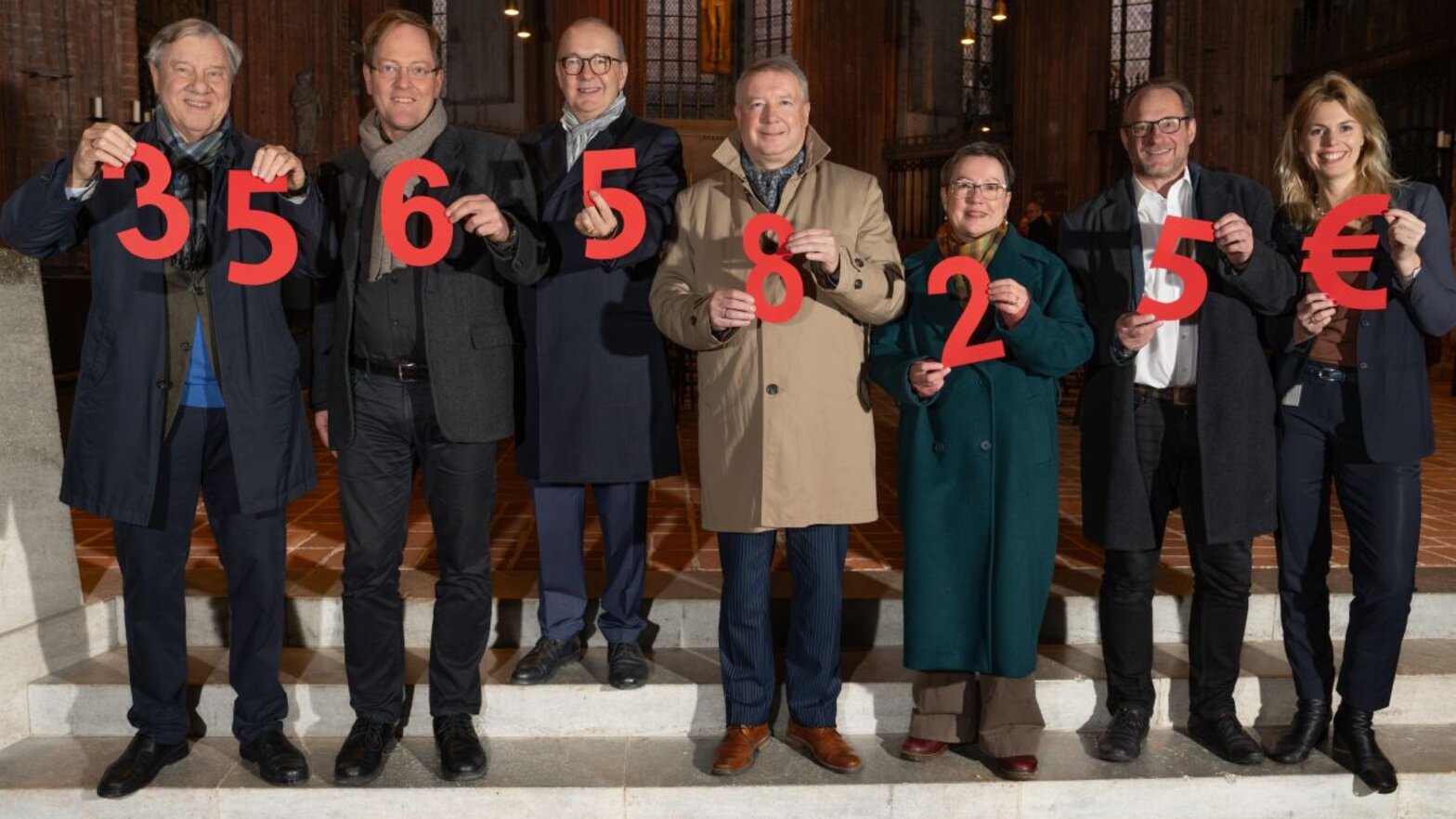 Sieben Menschen halten Ziffern in den Händen, die gemeinsam die Spendensumme ergeben