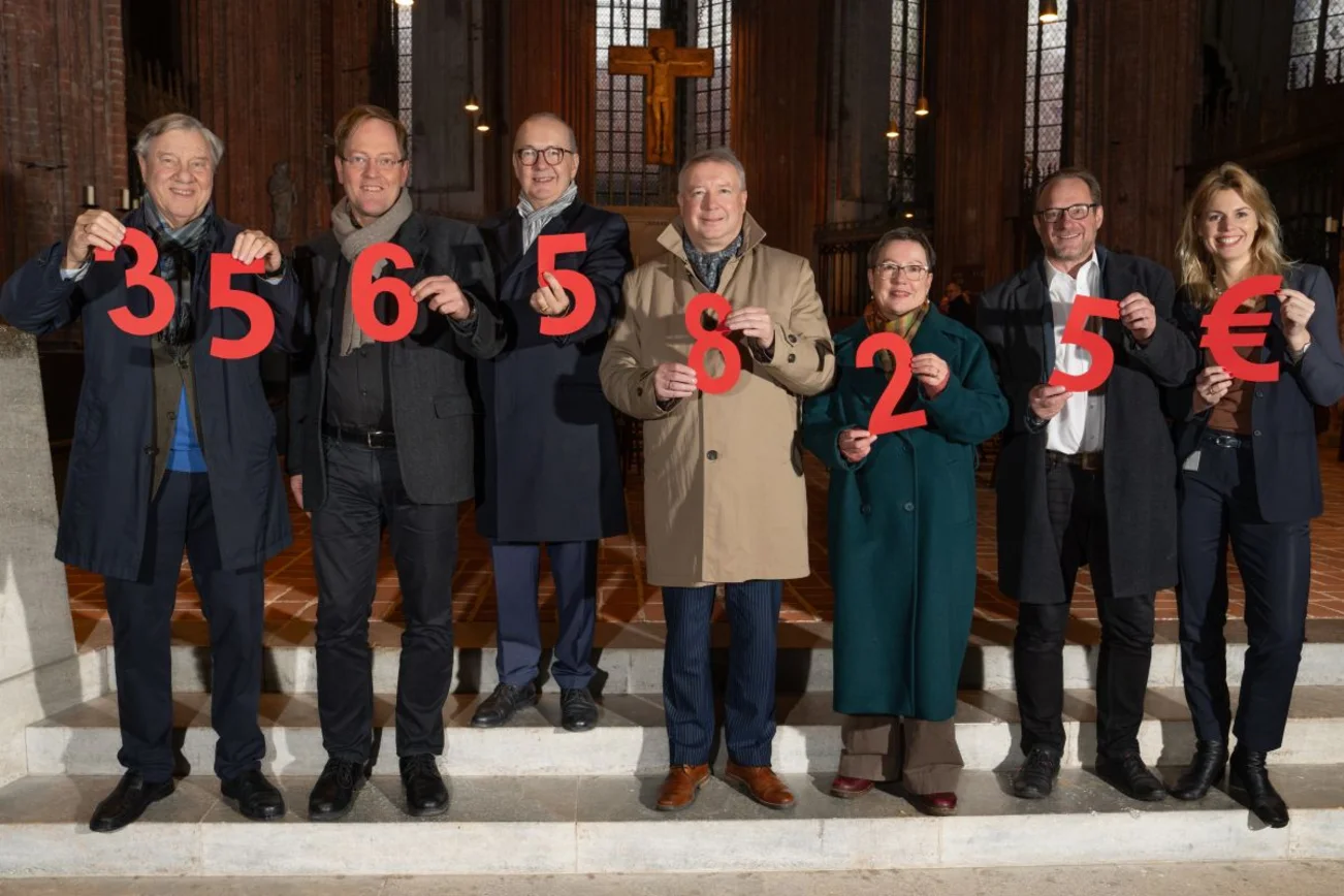 Sieben Menschen halten Ziffern in den Händen, die gemeinsam die Spendensumme ergeben