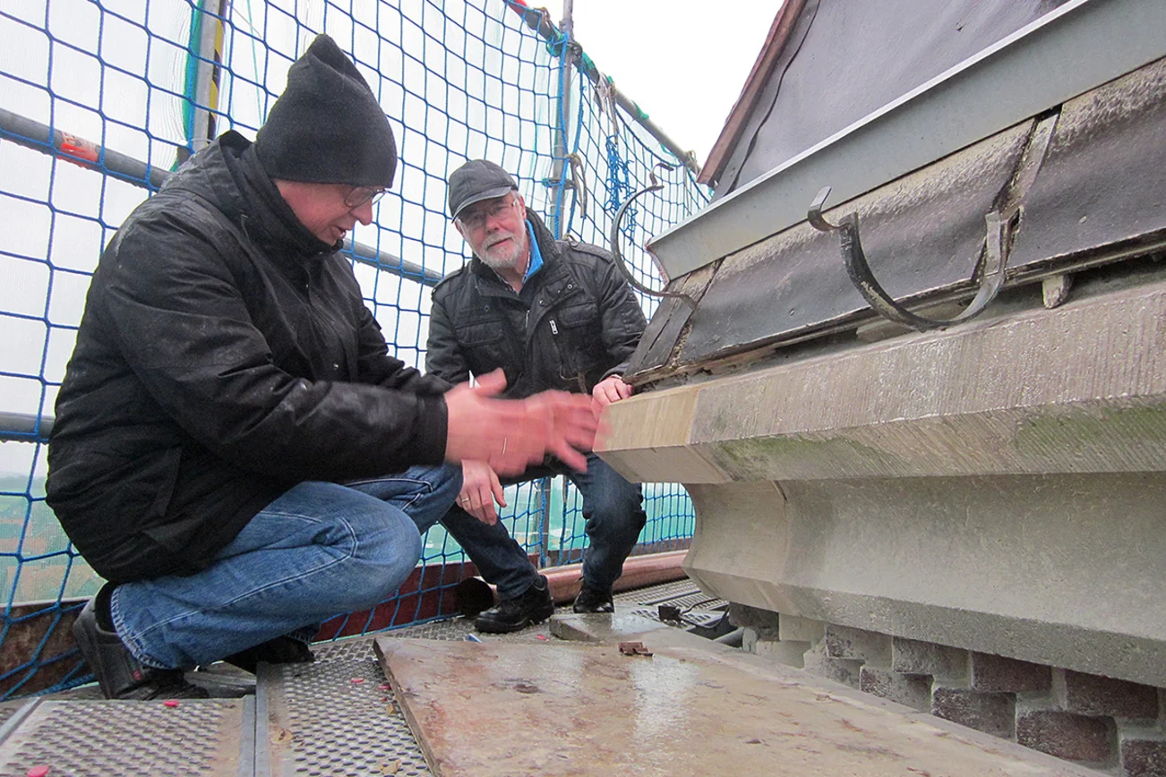 Werner Grage (li.) und Horst Diestel an der Traufe des Turmes (Übergang von Turmstumpf zum Turmhelm). Hier ist das bereits durch den Steinmetz reparierte Sandsteintraufgesims zu sehen und die lose Kupferblecheindeckung. Der untere Teil der Kupferblecheindeckung ist entfernt worden.