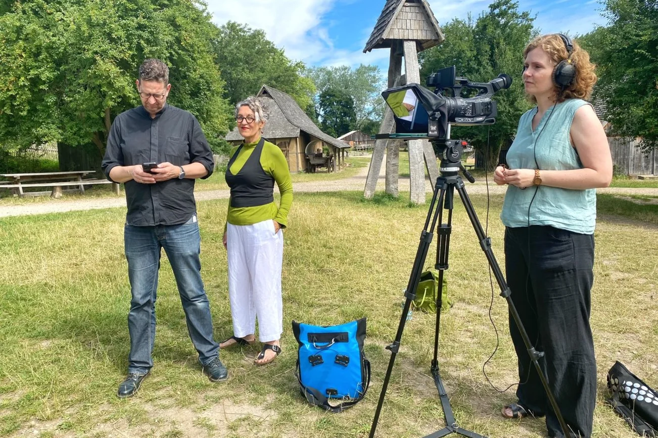 Drei Personen stehen hinter der Kamera. 