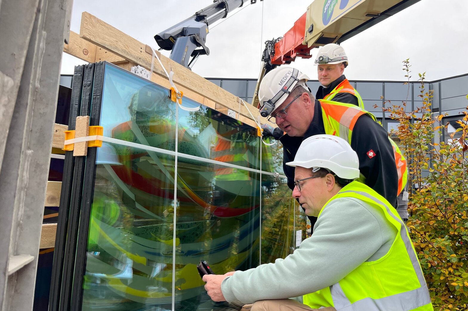 Drei Männer in Sicherheitskleidung vor den noch verpackten Fensterfronten.