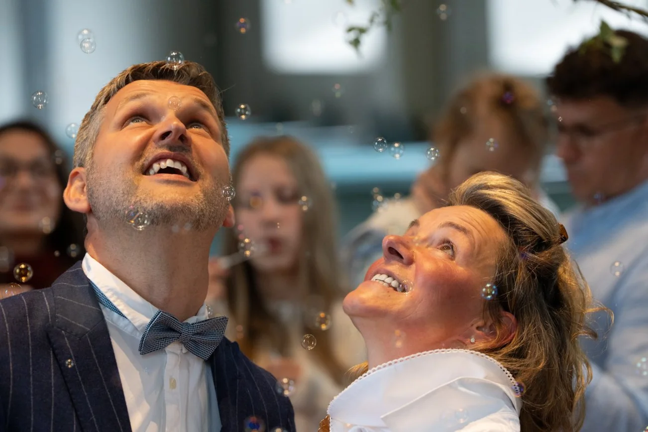 Ein Mann und eine Frau blicken lachend nach oben Seifenblasen hinterher.