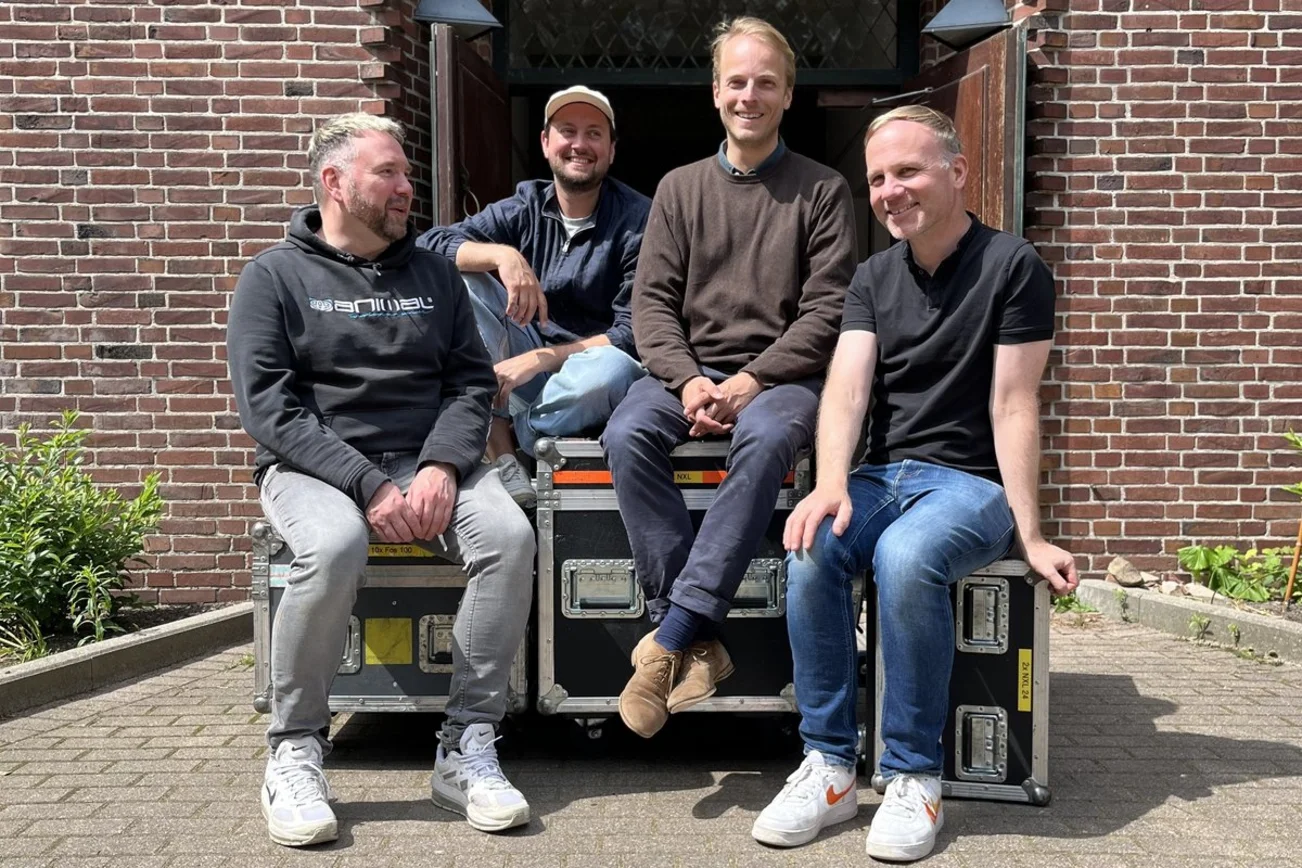 Vier Männer sitzen vor einer Kirche auf Technik-Containern.