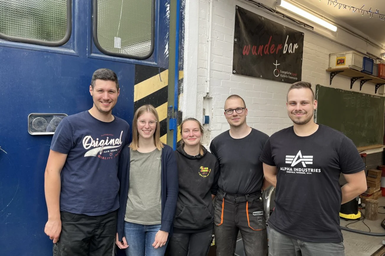 Fünf junge Menschen stehen am Eingang einer Werkstatt