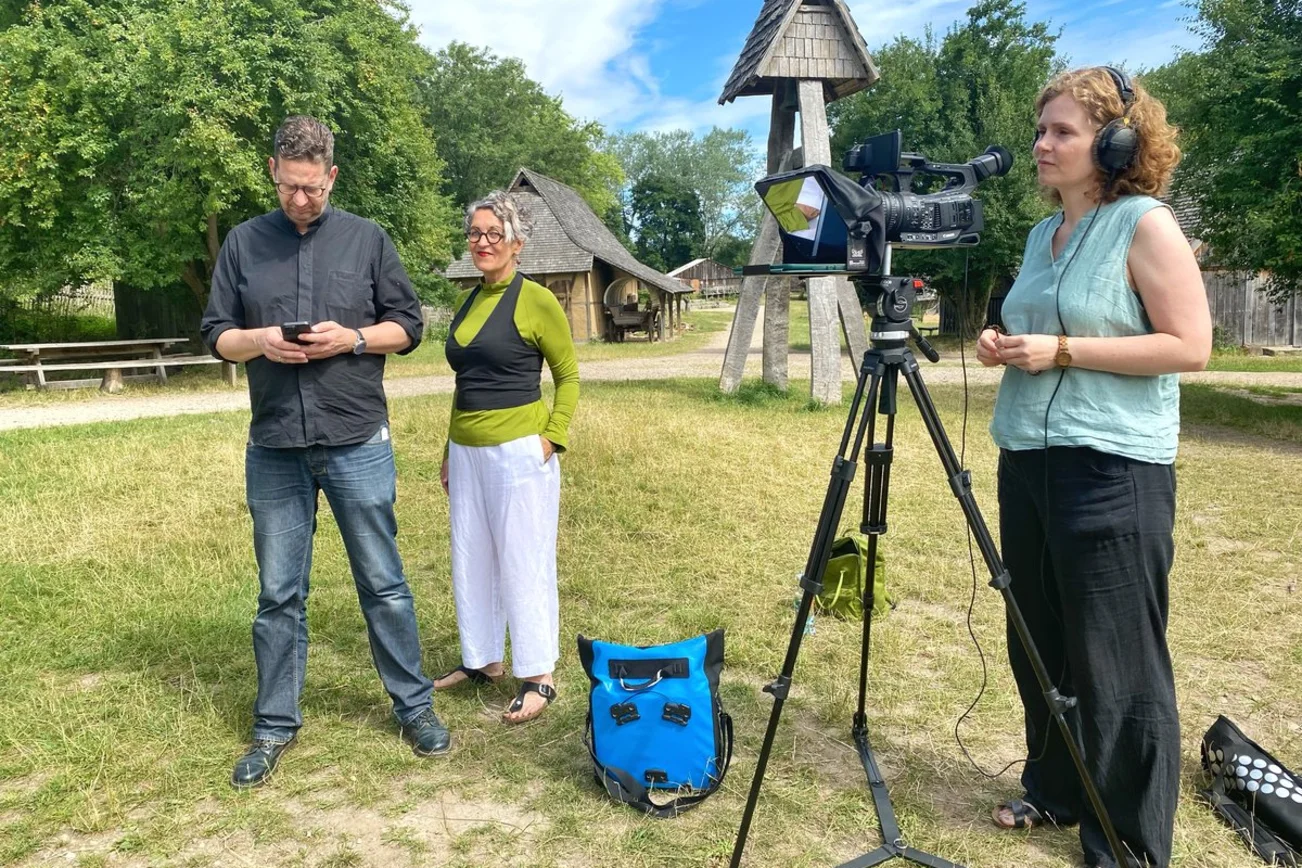 Drei Personen stehen an einer Kamera. 