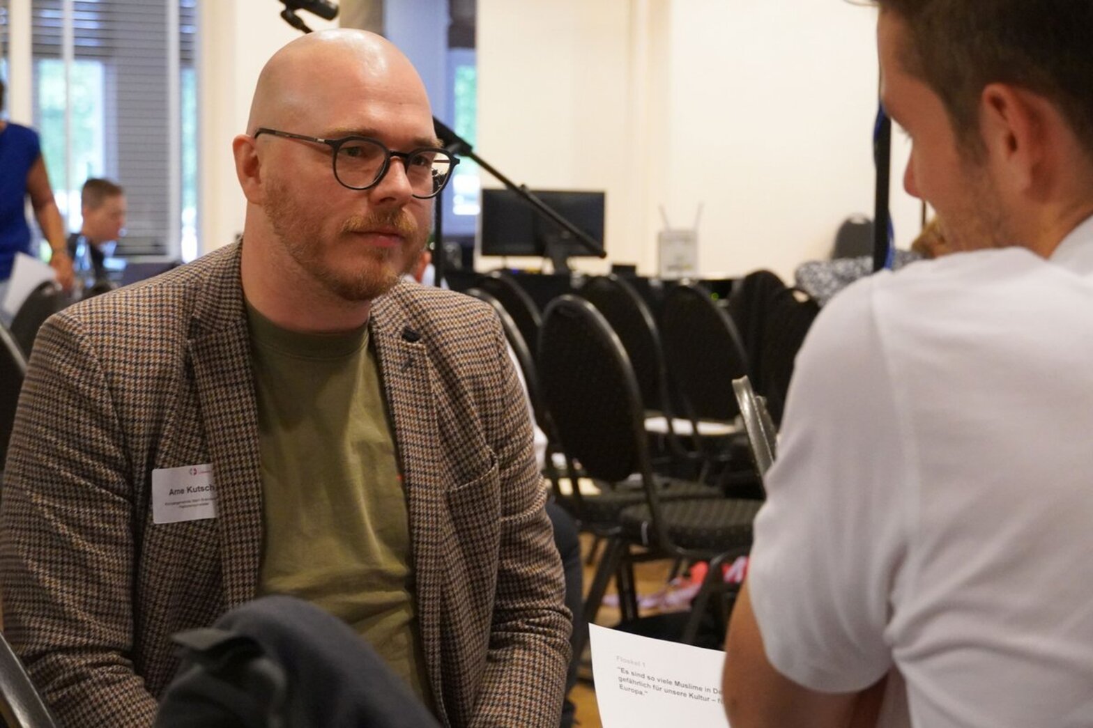 Ein Mann spricht mit einer anderen Personen die man nur von hinten sieht.