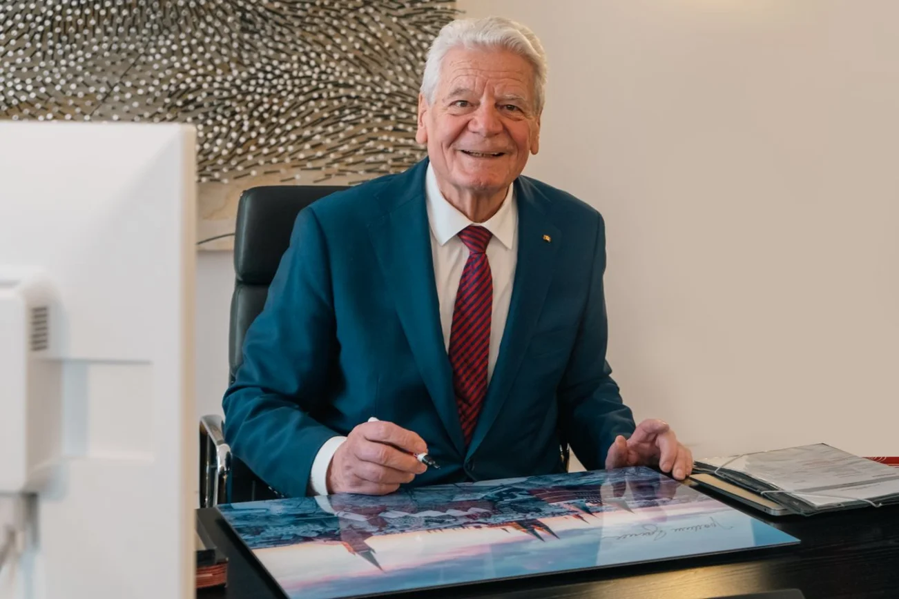 Ein Mann sitzt lächelnd an einem Schreibtisch. 