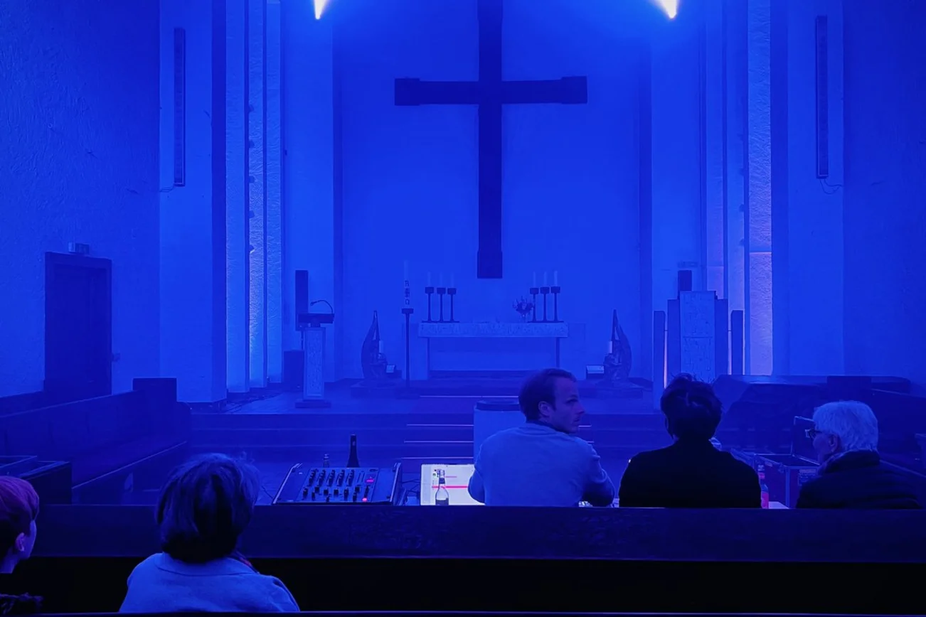 Ein blau erleuchteter Kirchenraum mit einem Kreuz.
