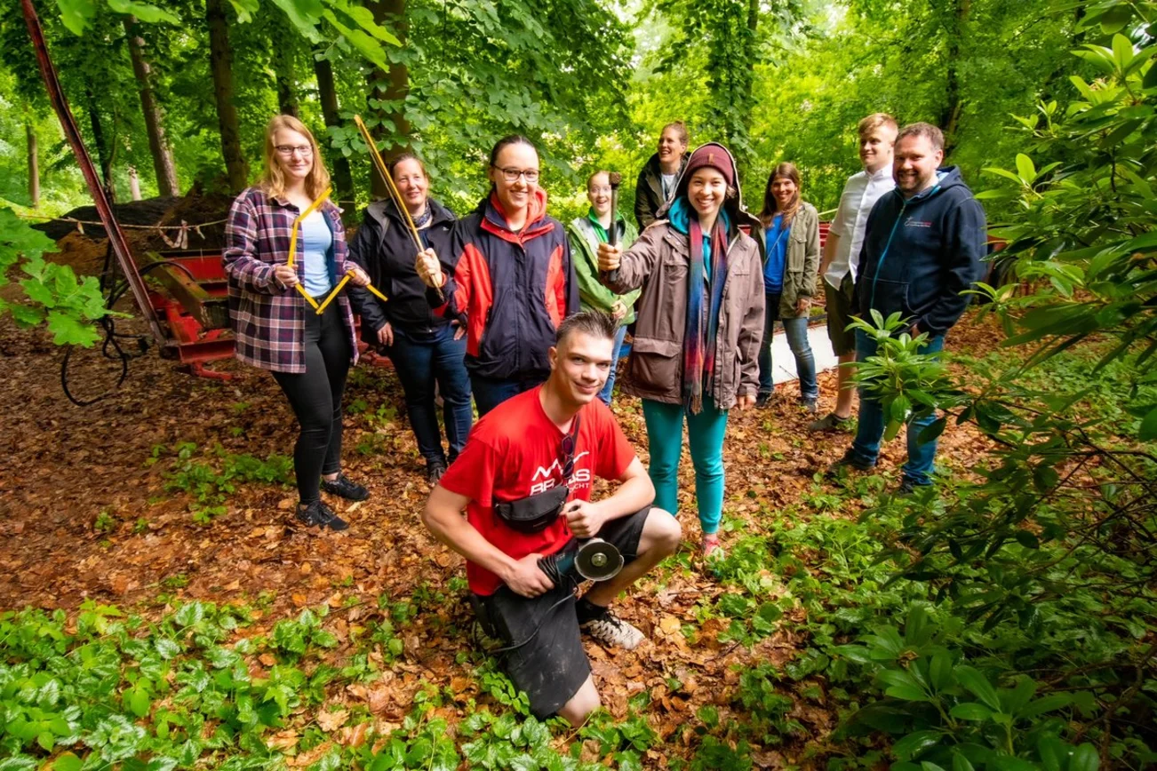 Eine Gruppe junger Menschen steht vor dem Auflieger eines Anhängers im Wald. 