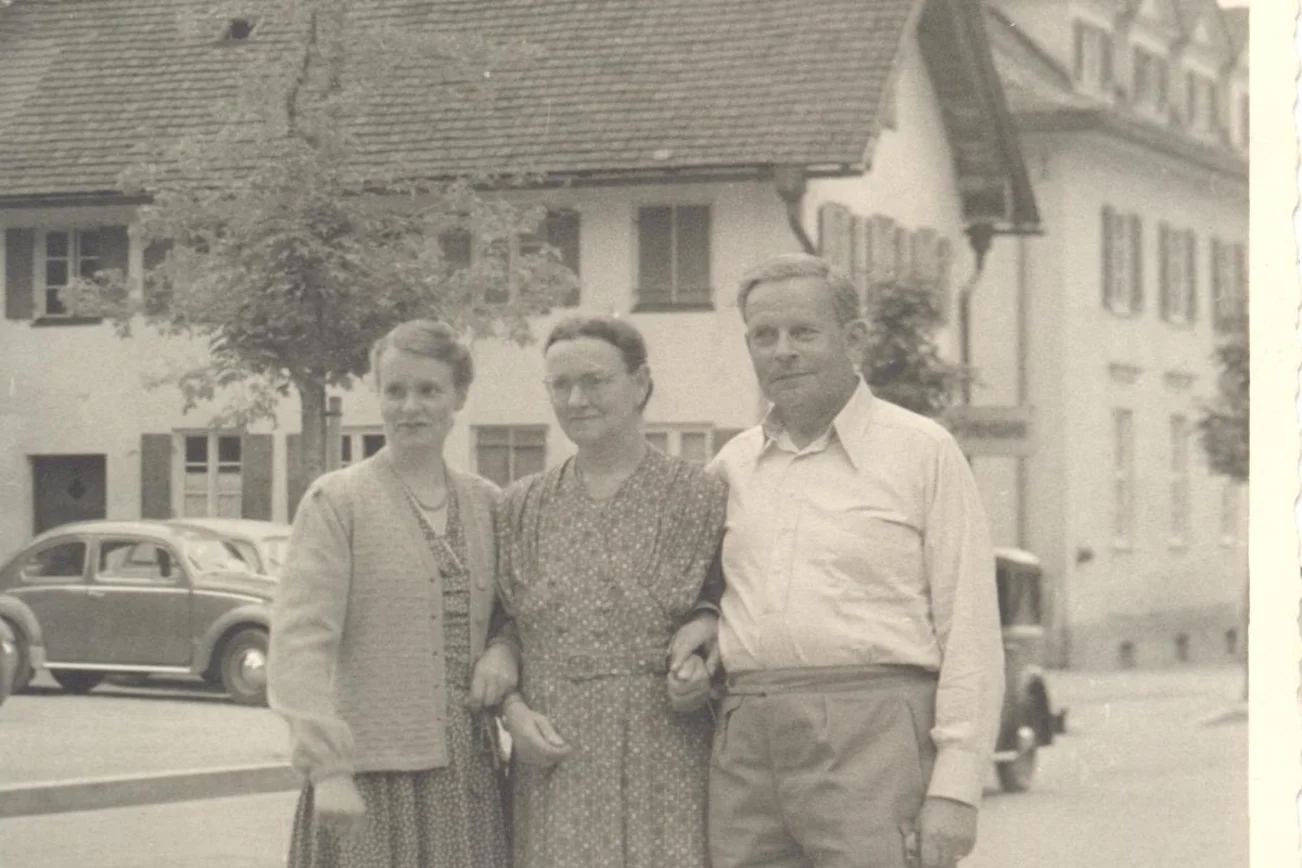 Ein historisches Foto. Drei Menschen sind zu sehen. Sie stehen eingeharkt nebeneinander.