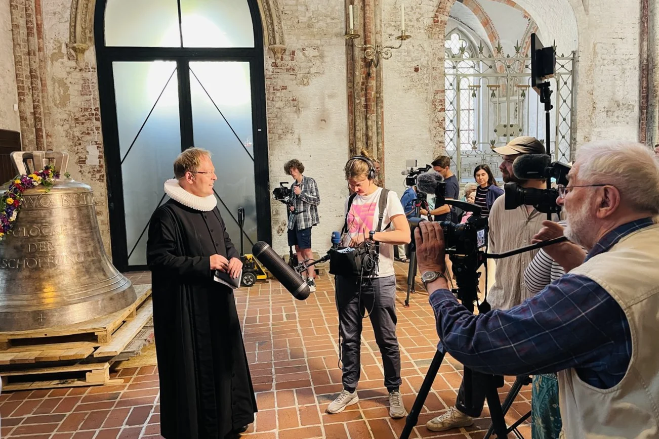 Ein Pastor steht vor Kameras in einer Kirche. 
