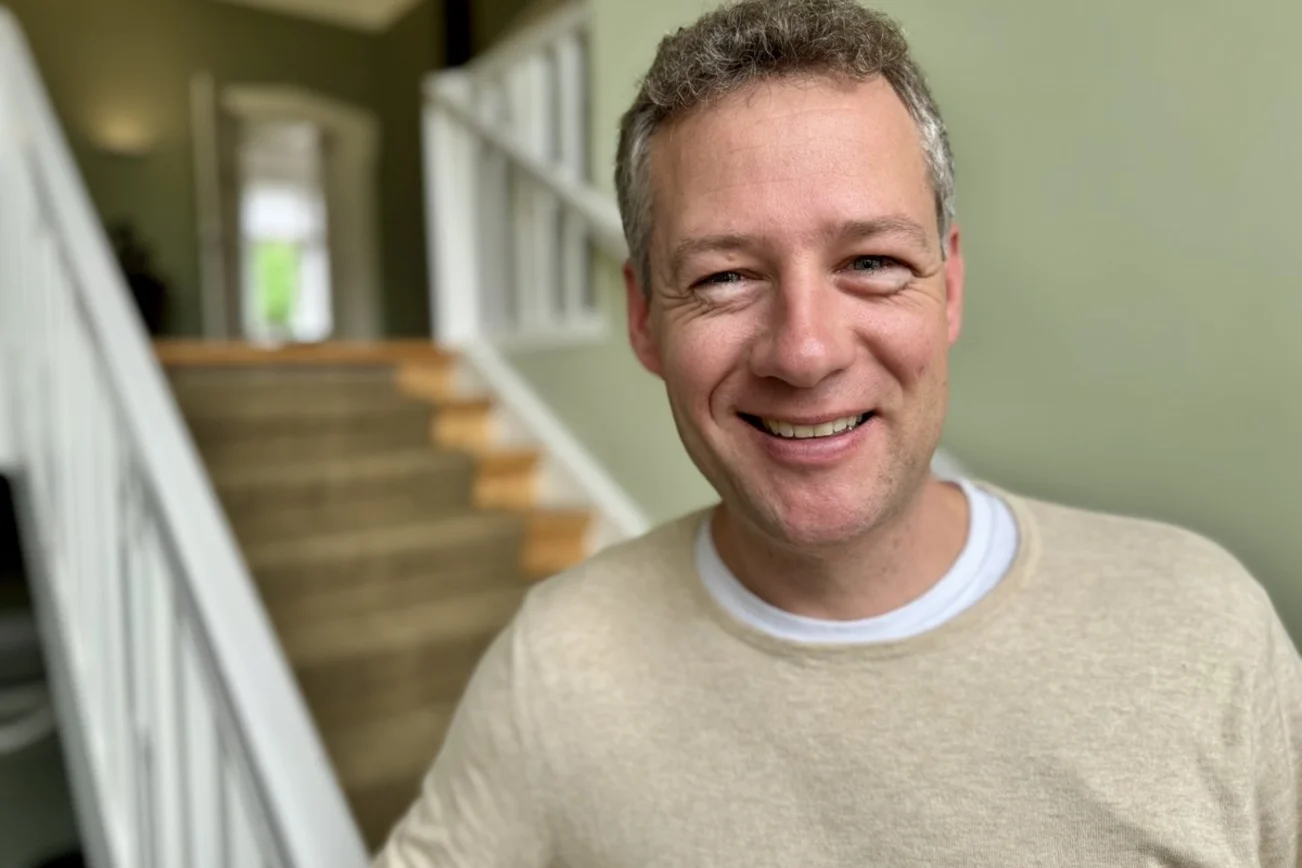 Junger Mann steht in die Kamera lächelnd auf der Treppe.