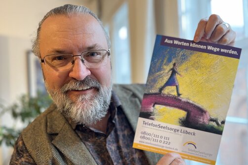 Ein Mann hält lächelnd ein Plakat in die Kamera. 