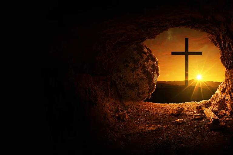 Blick aus einer dunklen Höhle, ein Stein liegt weggerollt auf der linken Seite. Im Sonnenaufgang sieht man ein großes Kreuz.