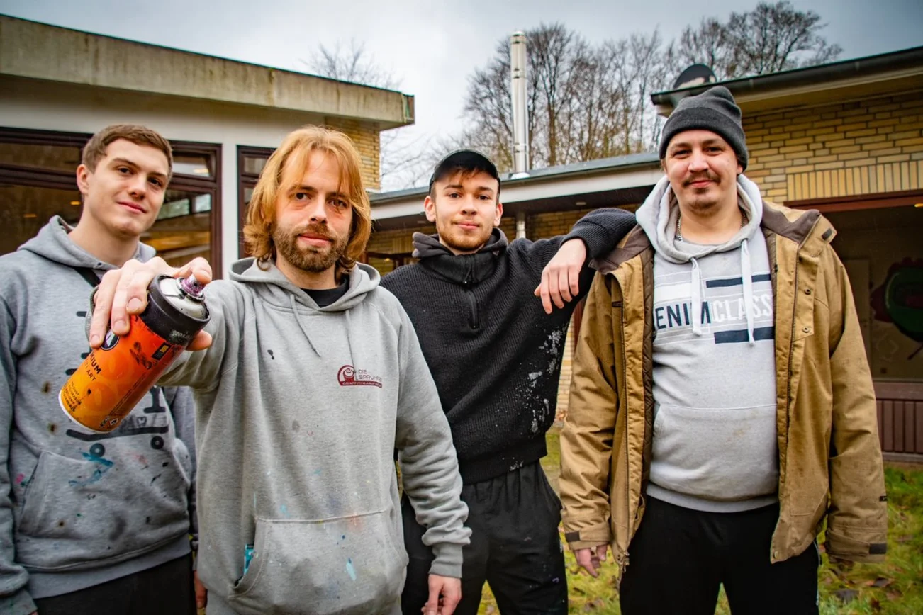 Eine Gruppe junger Männer steht mit Sprayflaschen vor dem alten Gemeindehaus in Wohltorf.