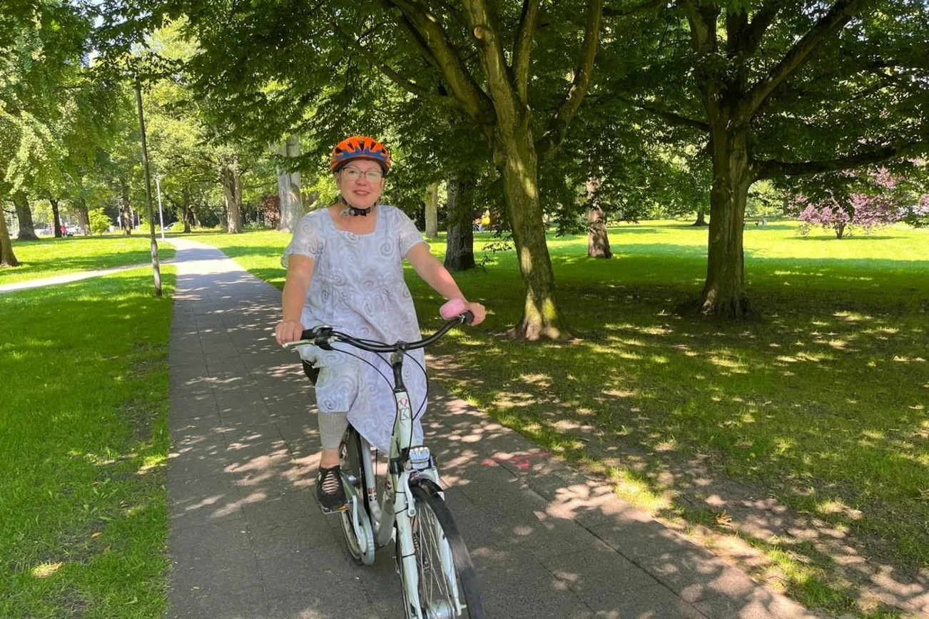 Pröpstin Kallies sitzt mit einem Fahrradhelm auf dem Kopf in einem begrünten Park auf dem Fahrrad.