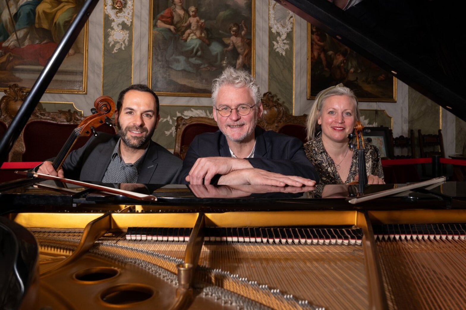 Drei Musiker sitzen hinter einem geöffneten Klavier.
