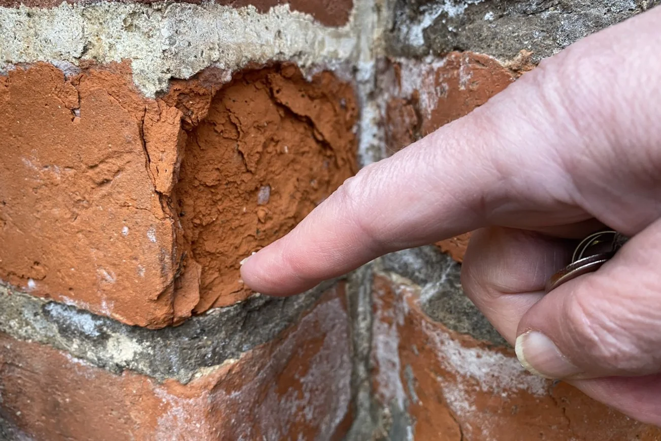 Eine Hand zeigt auf einen bröselnden Stein im Mauerwerk.