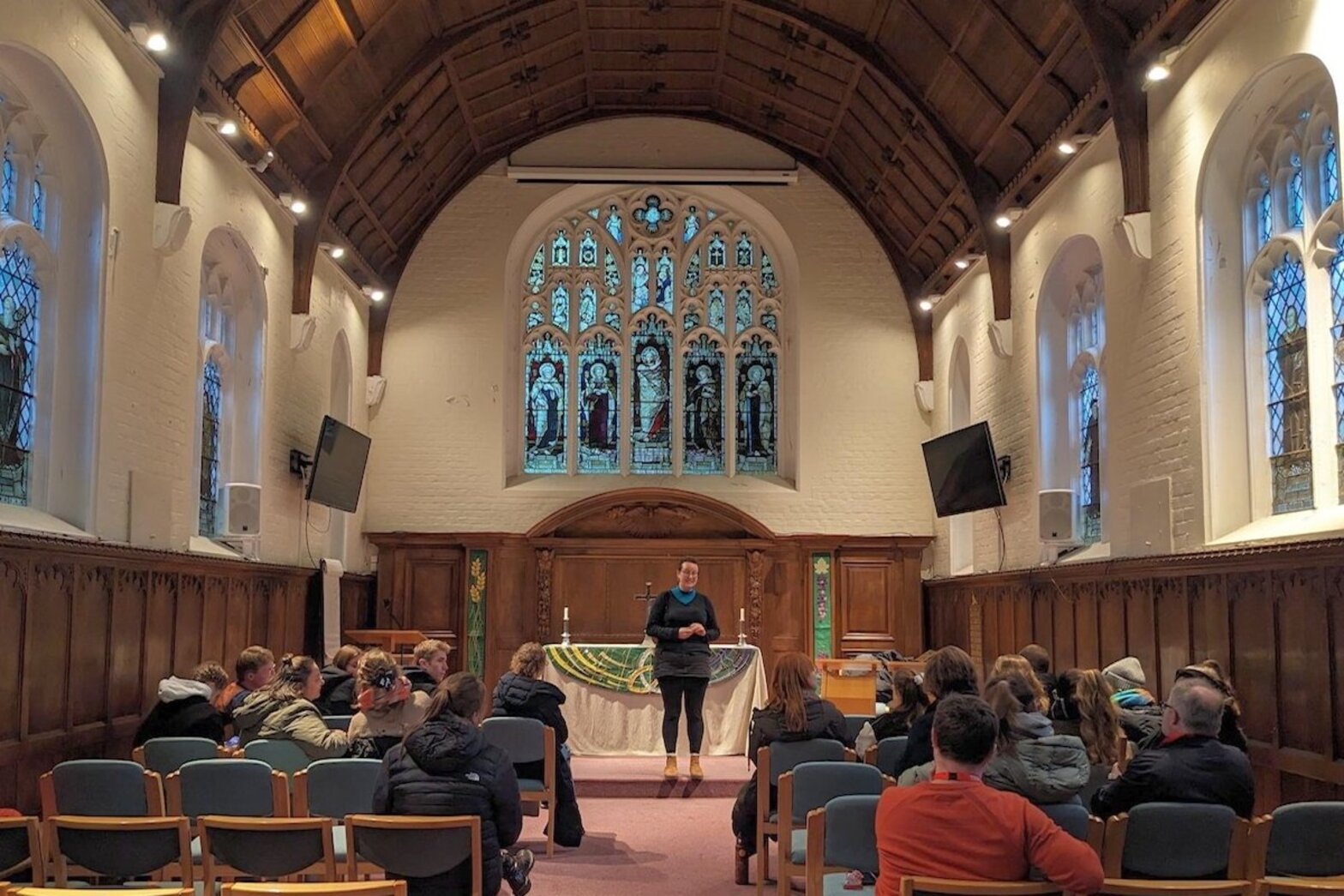 Eine Person steht in einer Kapelle vor mehreren Menschen.