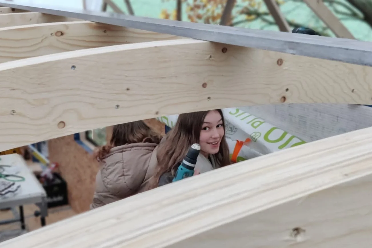 Eine junge Frau schaut zwischen den Deckenbalken eines Bauwagens hervor.