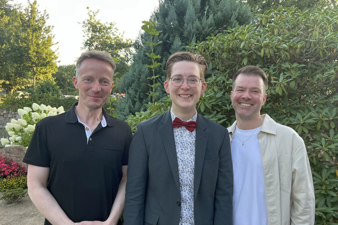 Drei Männer stehen draußen und lächeln für die Kamera.