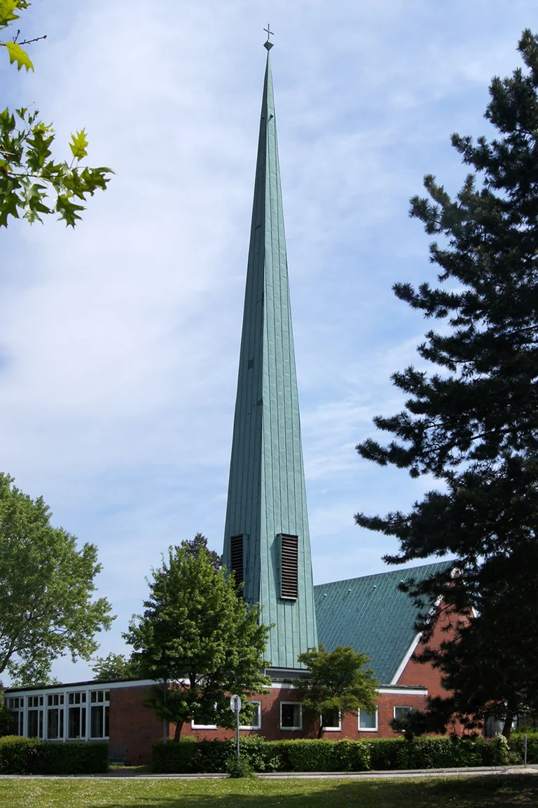 sehr hoher, spitzer Glockenturm mit Kupferblech, rechts Kirche, unten Gemeinderäume          