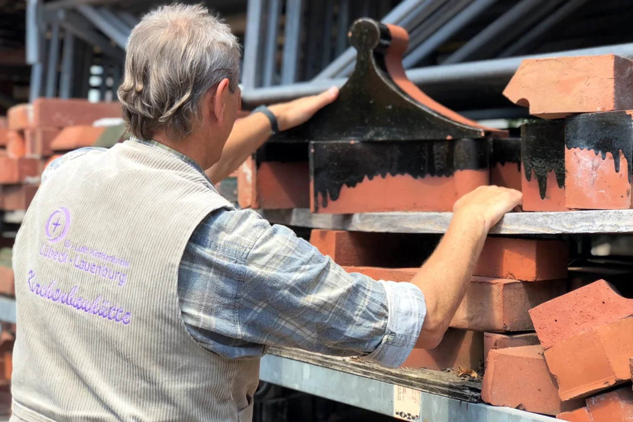Ein Bauregal mit verschiedenen Backsteinen- Links im Bild die Rückansicht eines Mannes. 