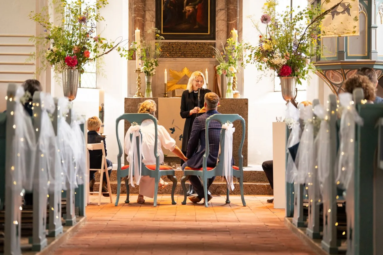 Blick durch den Mittelgang einer Kirche auf ein Brautpaar und Pastorin am Altar.