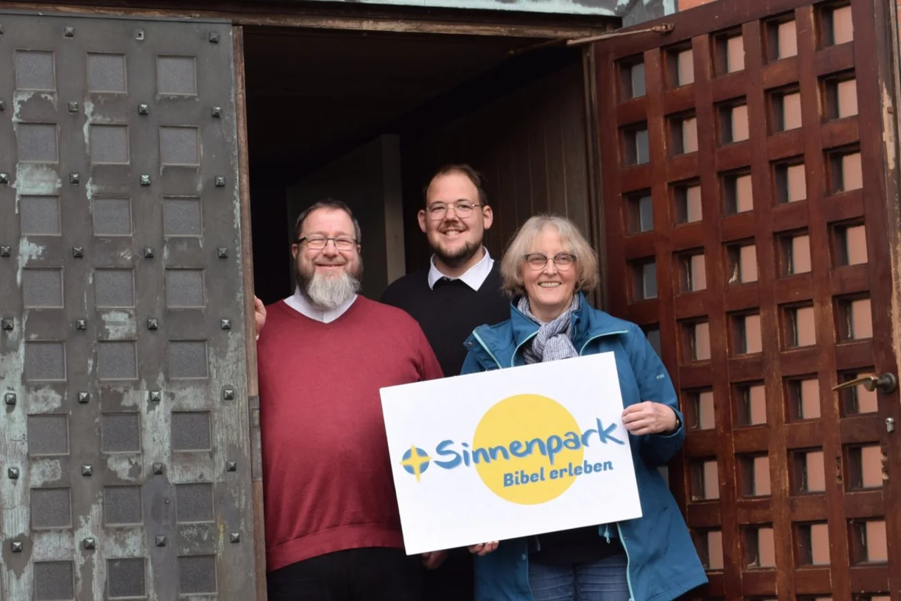 Drei Personen stehen im Eingang einer Kirche.