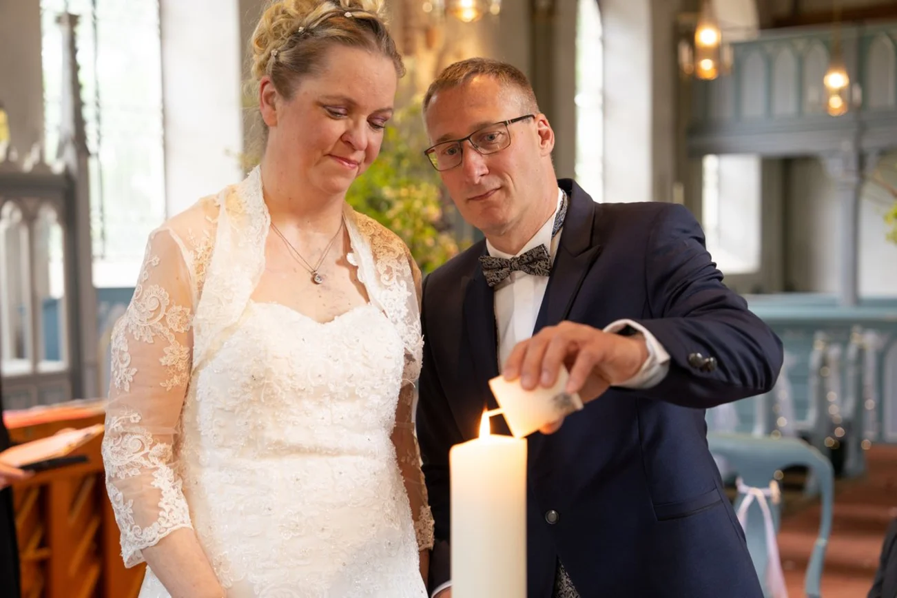 Ein Brautpaar steht vor einer Kerze. Der Mann entzündet ein Licht an der Kerze.