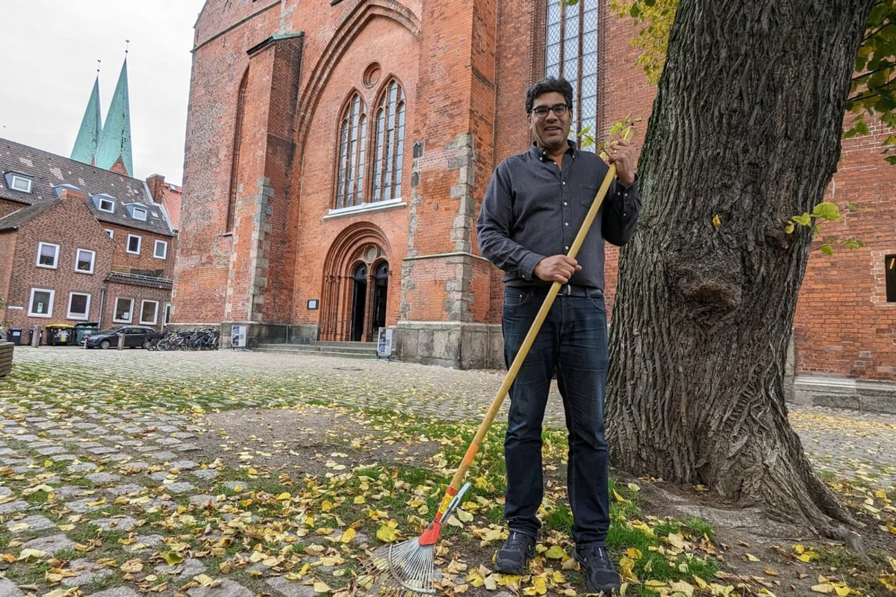 Ein Mann steht mit einem Rechen auf einem Kirchhof.