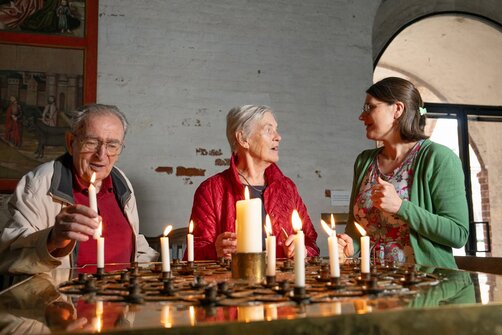 Ein älteres Paar steht mit einer jüngeren Frau an einem Kerzentisch. 