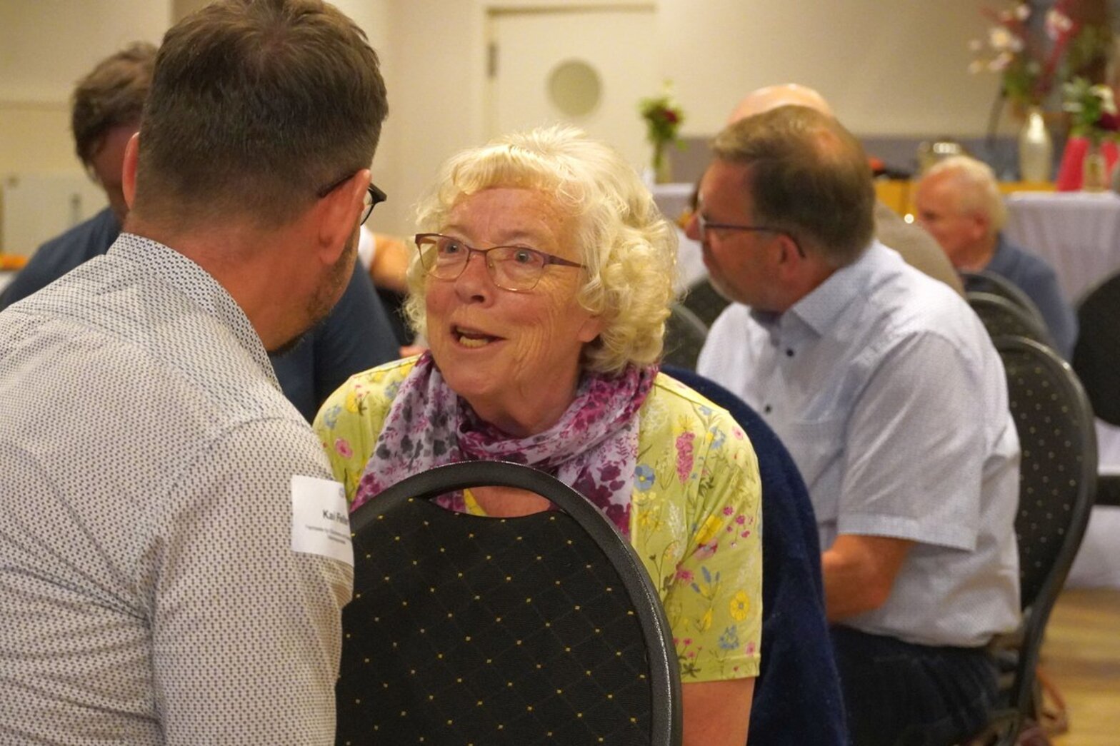 Eine Frau mit grauen Haaren und grünem Oberteil spricht mit einem Mann.