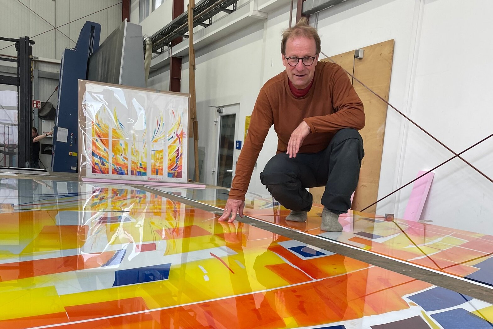 Ein Mann hockt auf den Glasfronten in der Glaswerkstatt.