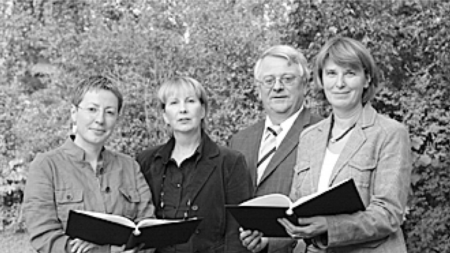 Vier Personen, drei Frauen, ein Mann stehen nebeneinander, links und rechts halten die Damen jeweils eine offene schwarze Mappe in den Händen