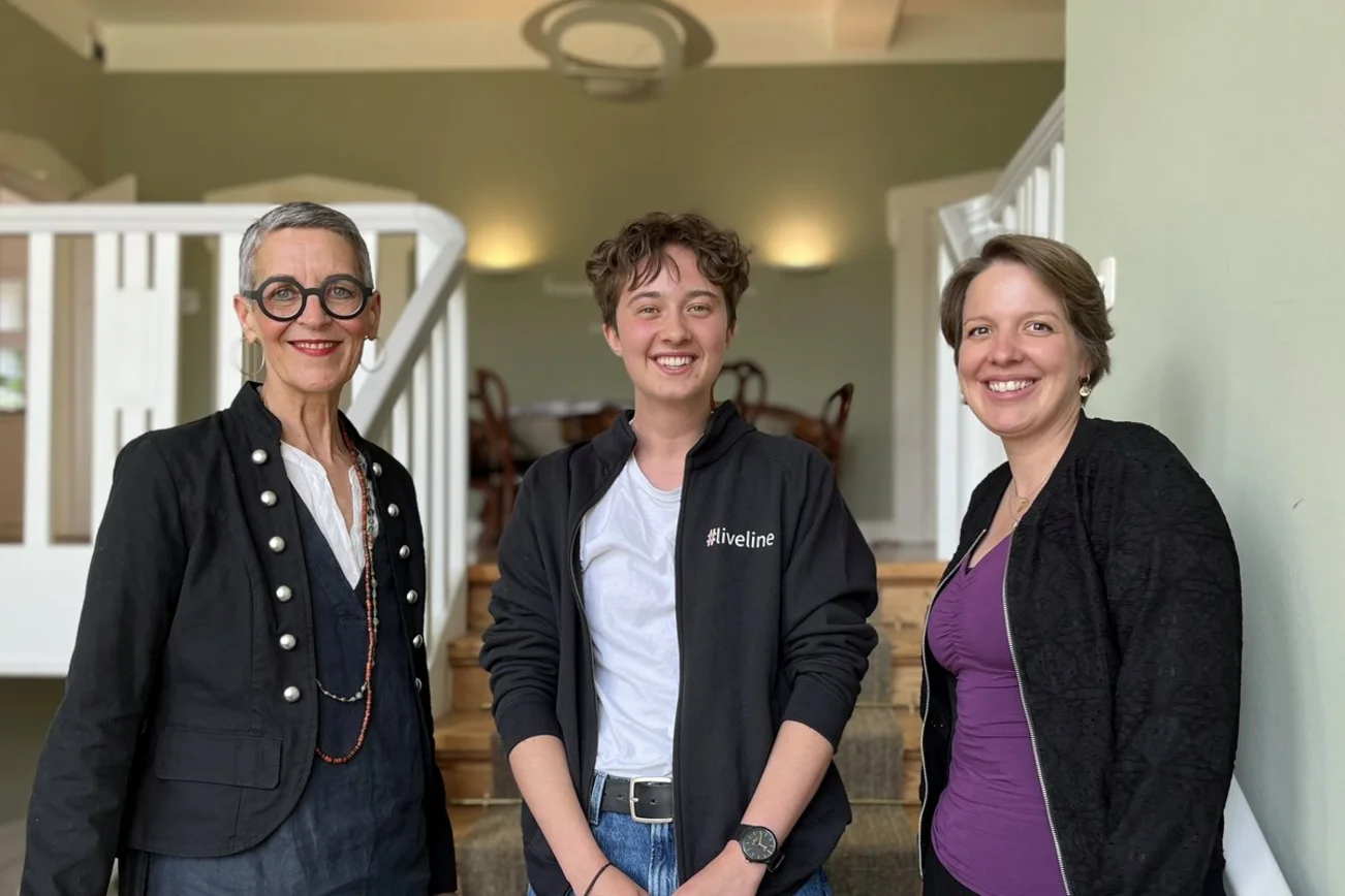 Zwei Frauen und ein junger Mann stehen auf einer Treppe und lächeln in die Kamera.