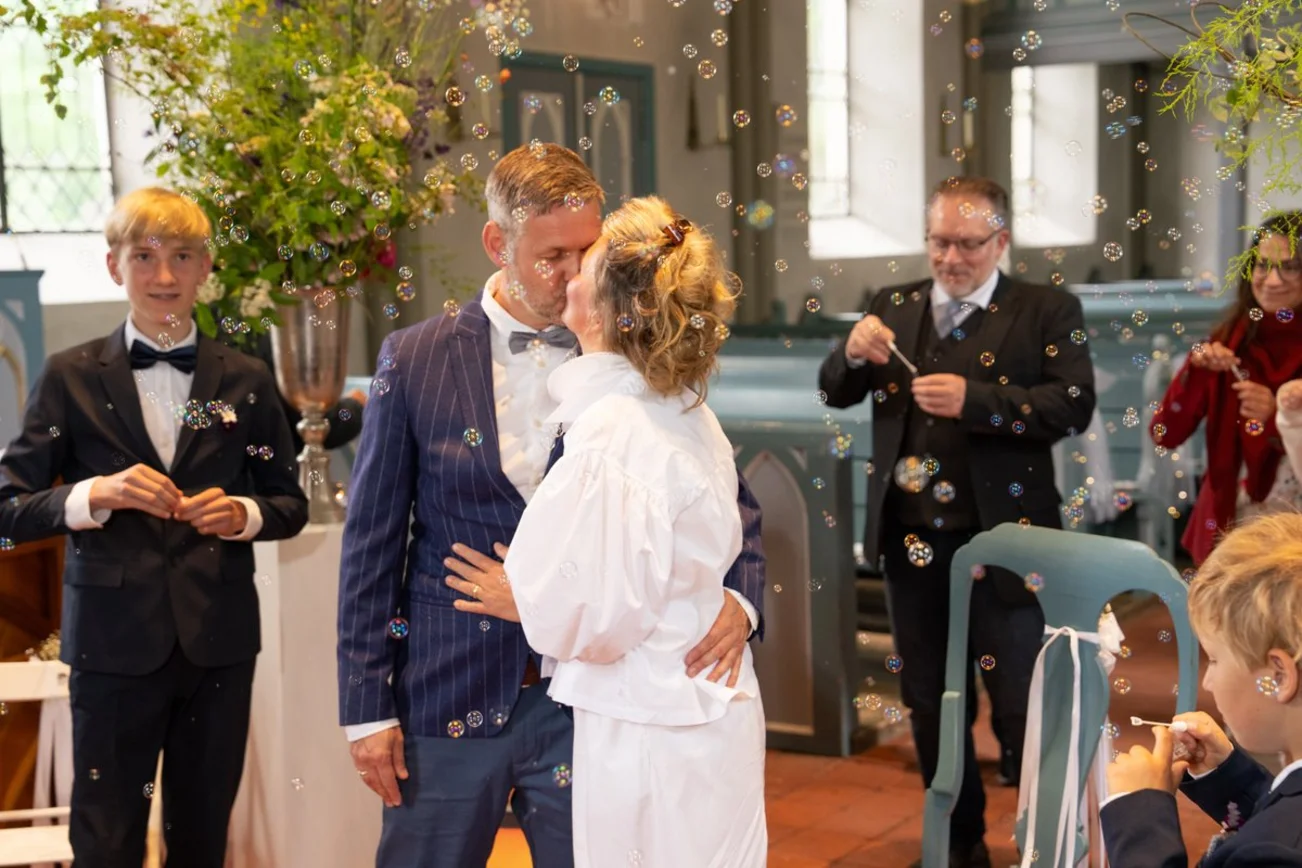 Ein Brautpaar küsst sich in einer Kirche inmitten von schwebenden Seifenblasen.