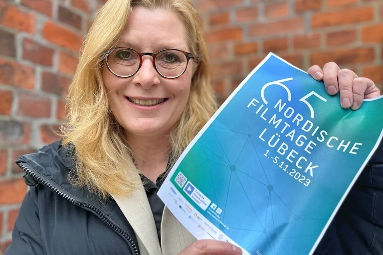 Eine Frau hält ein Plakat der Nordischen Filmtage in den Händen und blickt freundlich in die Kamera. 