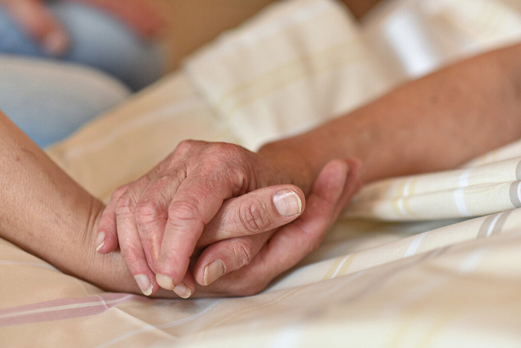 zwei Hände halten einander und liegen auf einer Bettdecke