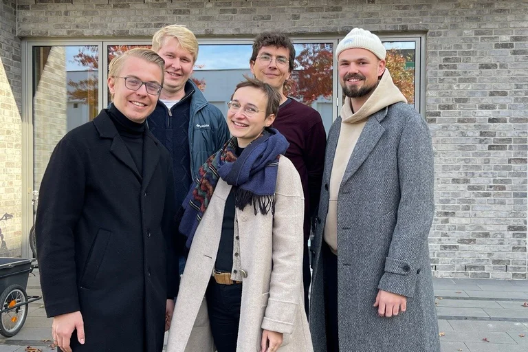 vier Männer und eine Frau stehen warm angezogen vor einem Backsteingebäude