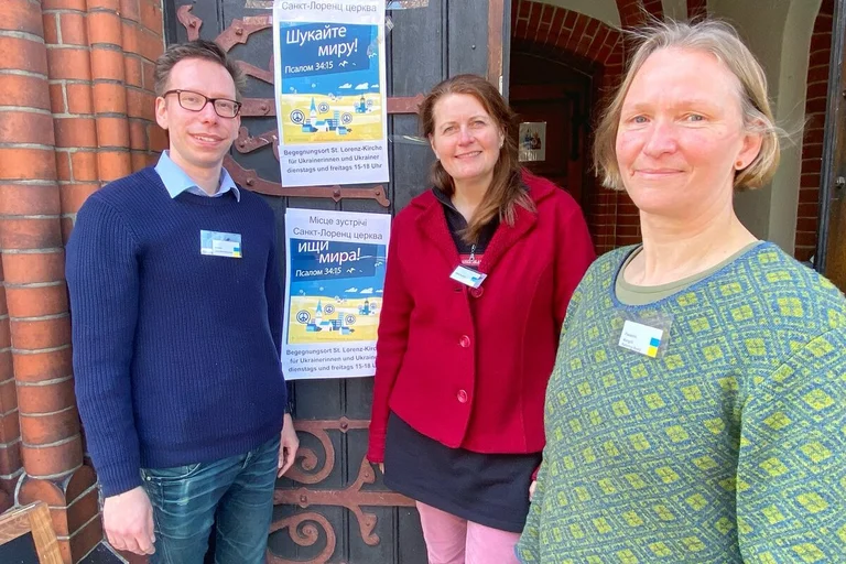 Drei Personen stehen vor dem Eingang einer Kirche. 
