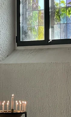 angezündete helle Kerzen unterhalb eines Kirchenfensters