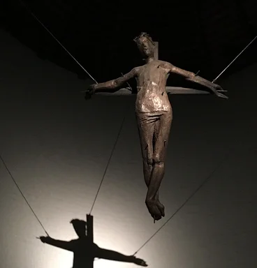 Im Altarraum hängt der gekreuzigte Christus, ein Licht erzeugt seinen Schatten auf der hinteren Wand des Altarraumessein Schatten 