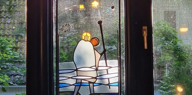 Ein Kirchenfenster zeigt einen Mann mit einem langen Stock, darüber gelbe Sterne