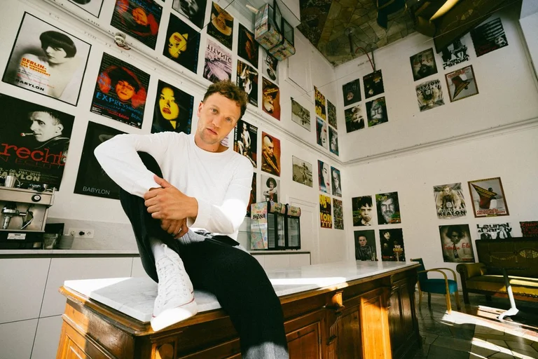 Ein junger Mann sitzt auf einem Tisch vor Wänden mit Plattencovern.