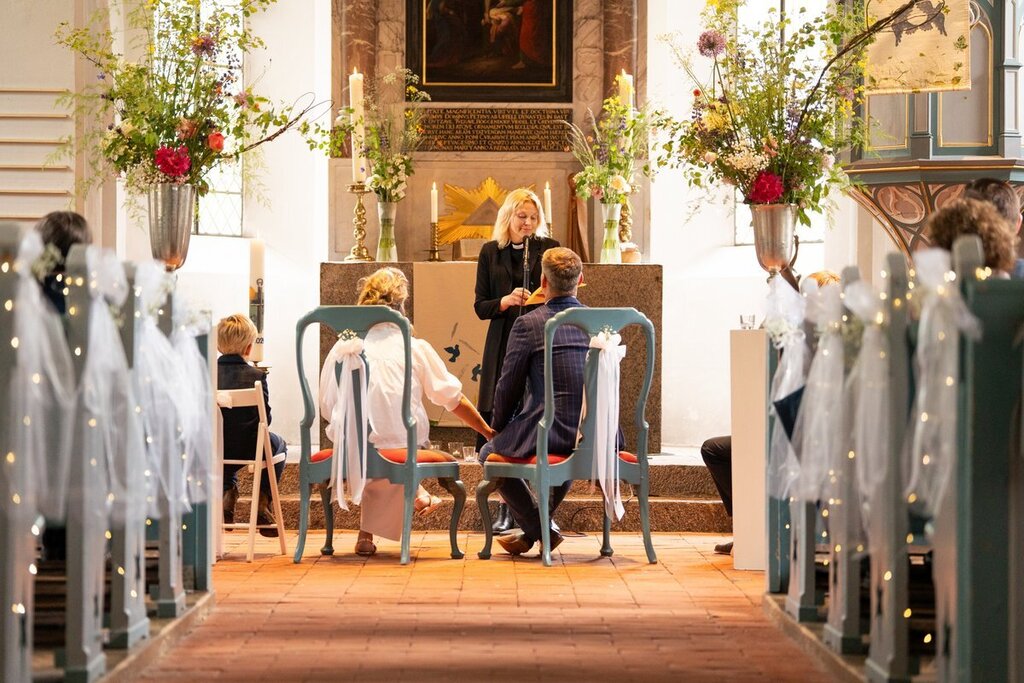 Blick in den geschmückten Mittelgang einer Kirche mit Brautpaar und Pastorin im Altarraum..