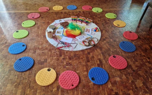 Mehrere Instrumente liegen im Kreis auf einer hellen Unterlagen, drum herum liegen bunte runde Sitzgelegenheiten